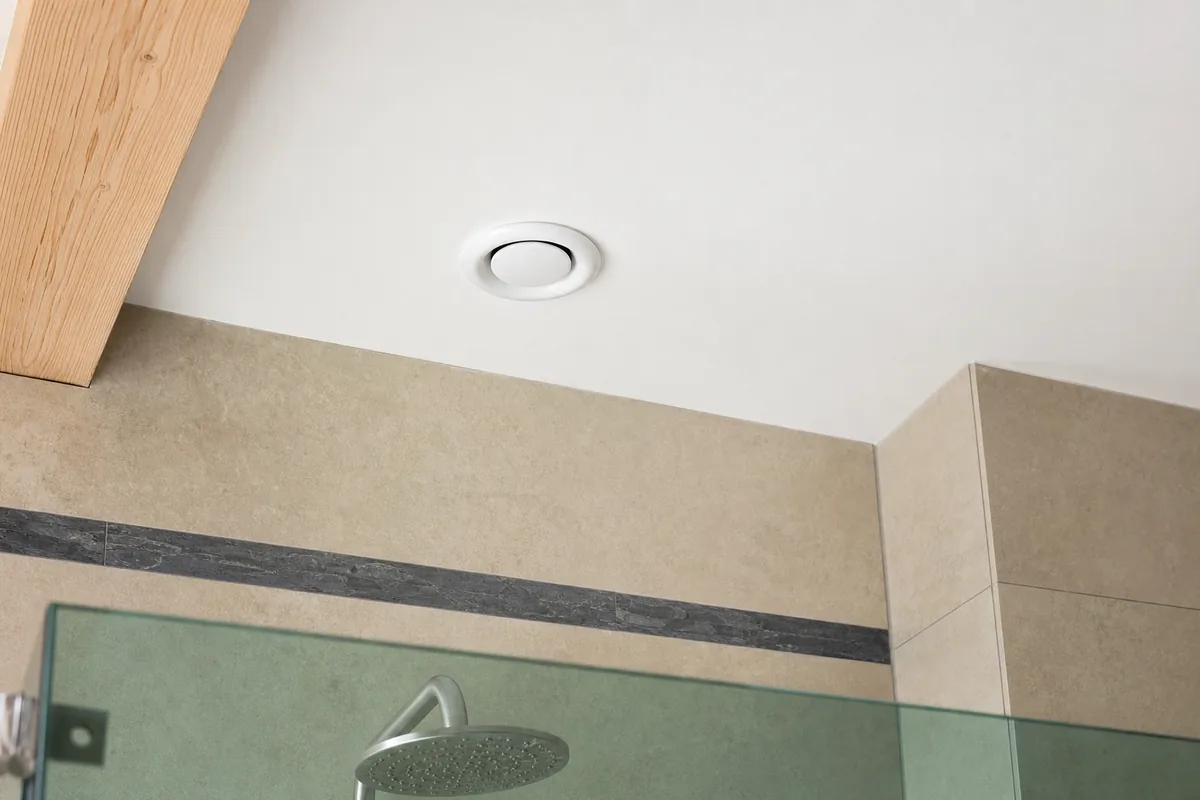 Bouche d&rsquo;extraction discrète au plafond d&rsquo;une salle d&rsquo;eau carrelée sable et gris