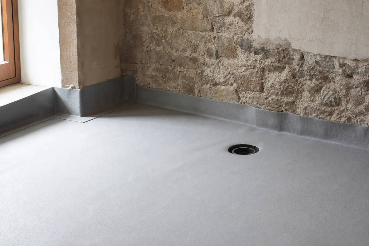 Plancher bois ancien renforcé recouvert d&rsquo;une natte d&rsquo;étanchéité claire, départ de mur en granite enduit à la chaux