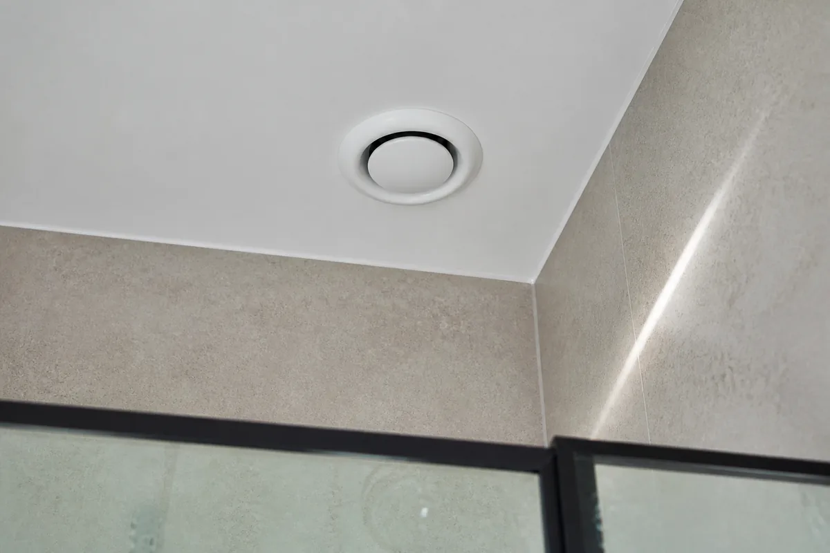 Bouche de ventilation hygroréglable au plafond d&rsquo;une salle d&rsquo;eau claire en carrelage sable