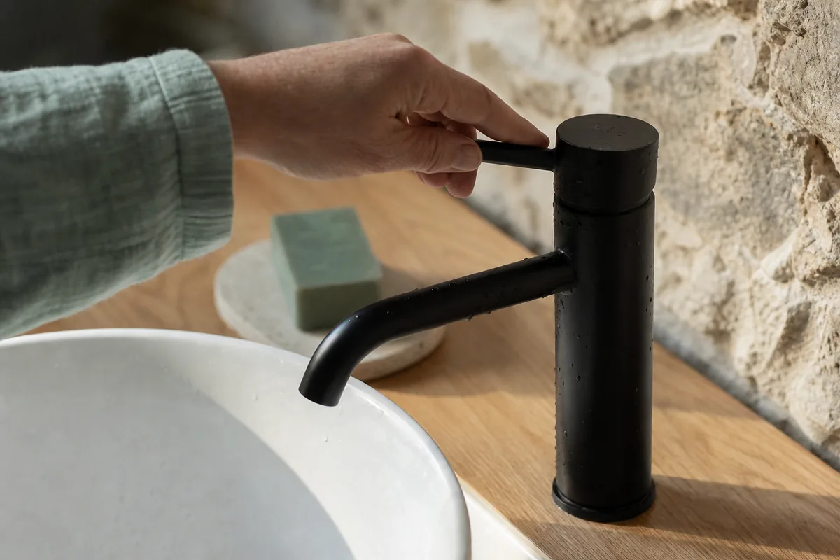 Robinetterie noire mate sur plan de vasque devant un mur de granite apparent